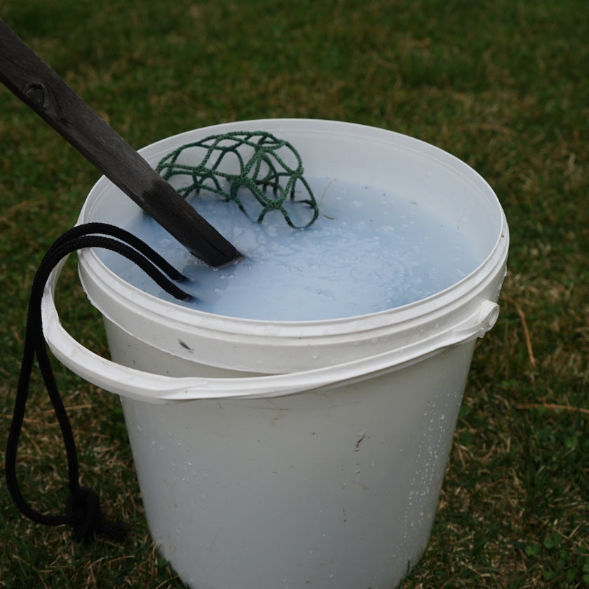 bucket of soapy water with a green hay net inside cleaning