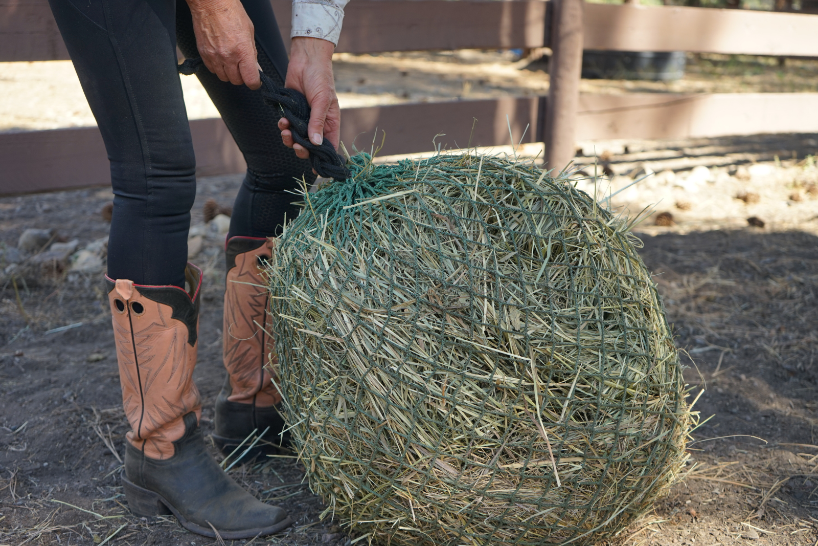 women tying up a hay net with pink boots