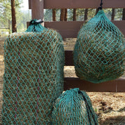 small square bale bale in a green net beside two flake feeding hay nets on a fence